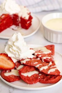 Red velvet waffles on a plate with cream cheese glaze and whipped cream on top.