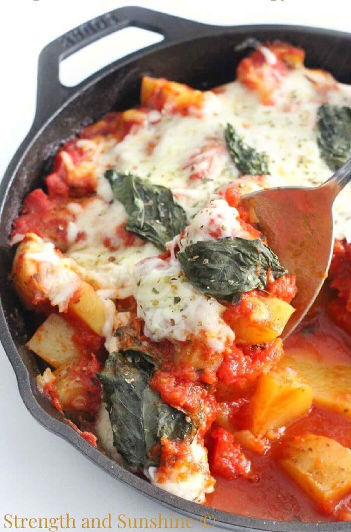 Potato casserole with cheese and tomato sauce topped with basil in a cast iron pan.