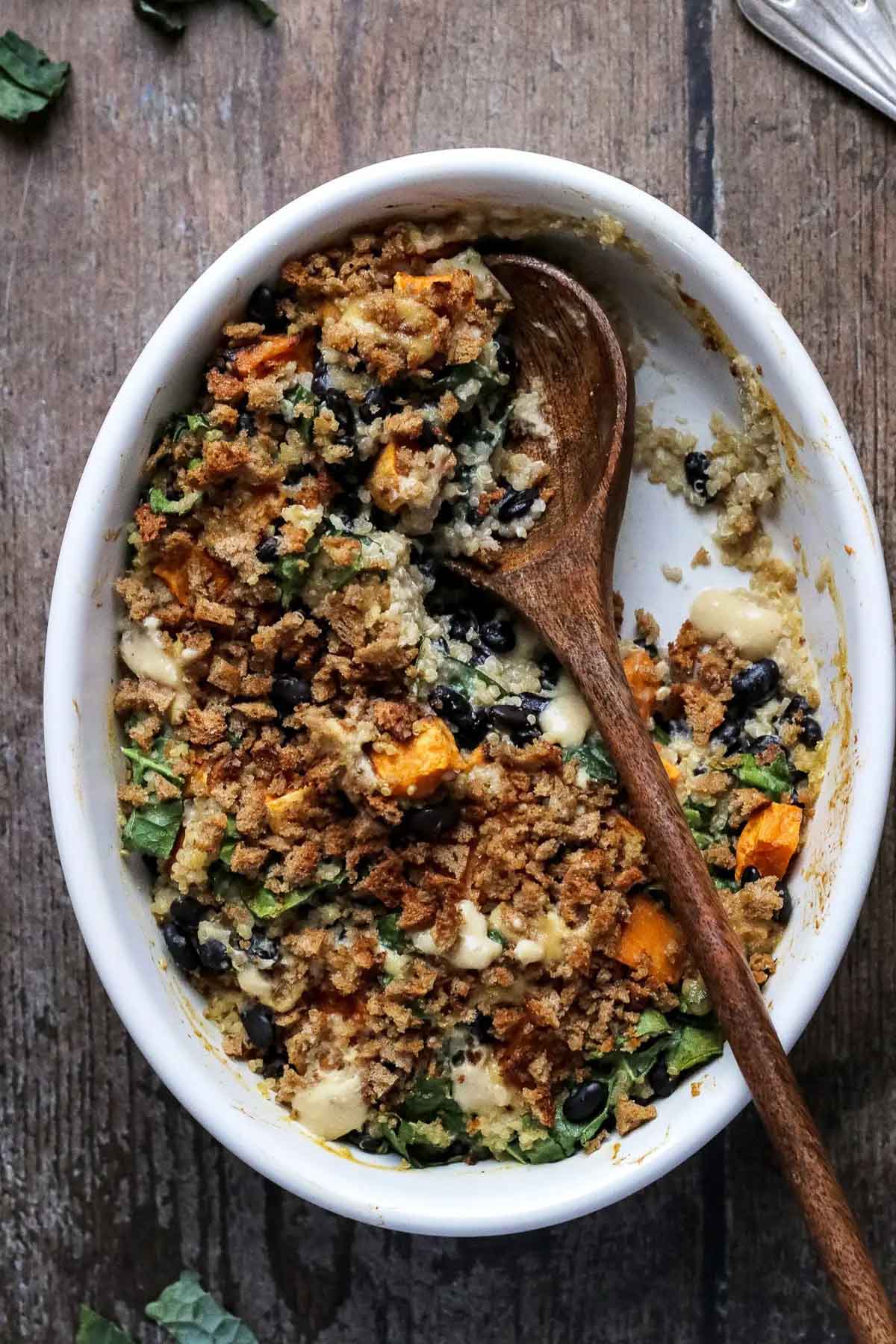 Sweet potato, black beans, kale and quinoa casserole in an oval dish with a wooden spoon in it.
