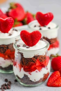 Glass jar full of layered strawberry breakfast parfait with heart shaped strawberry on top.