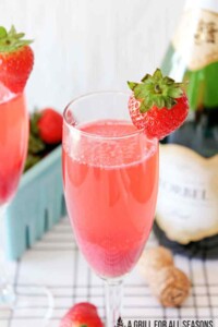 Pink strawberry mimosa in a champagne glass surrounded by strawberries.
