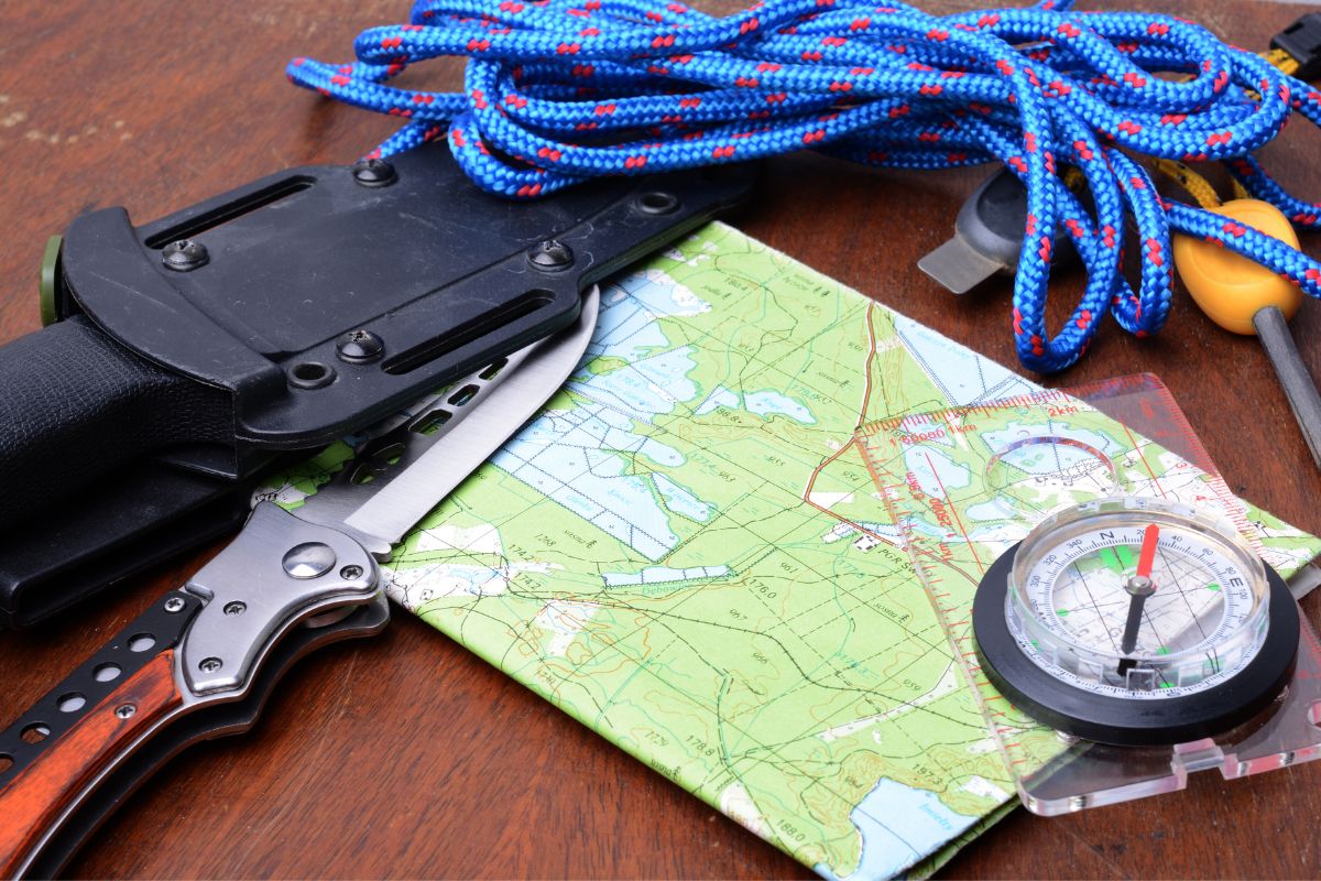 Map and compass on table next to knife and rope are part of a zombie survival kit.