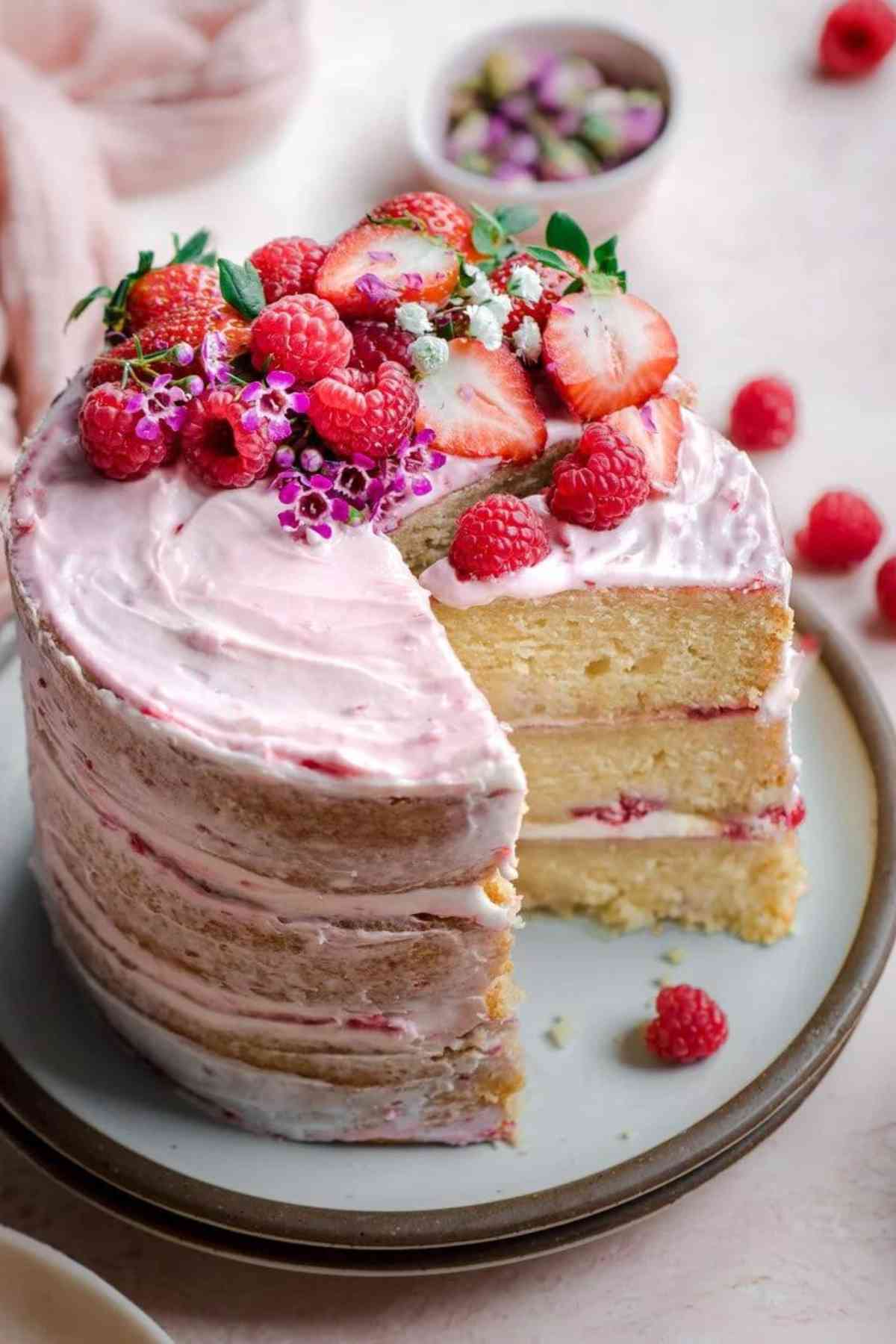 Three layer vanilla cake with layer of raspberry jam and pink frosting topped with berries.