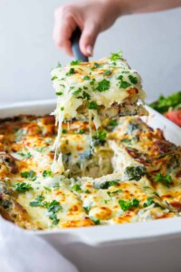 Slice of white chicken lasagna on a serving spatula hovering above a casserole dish of lasagna.