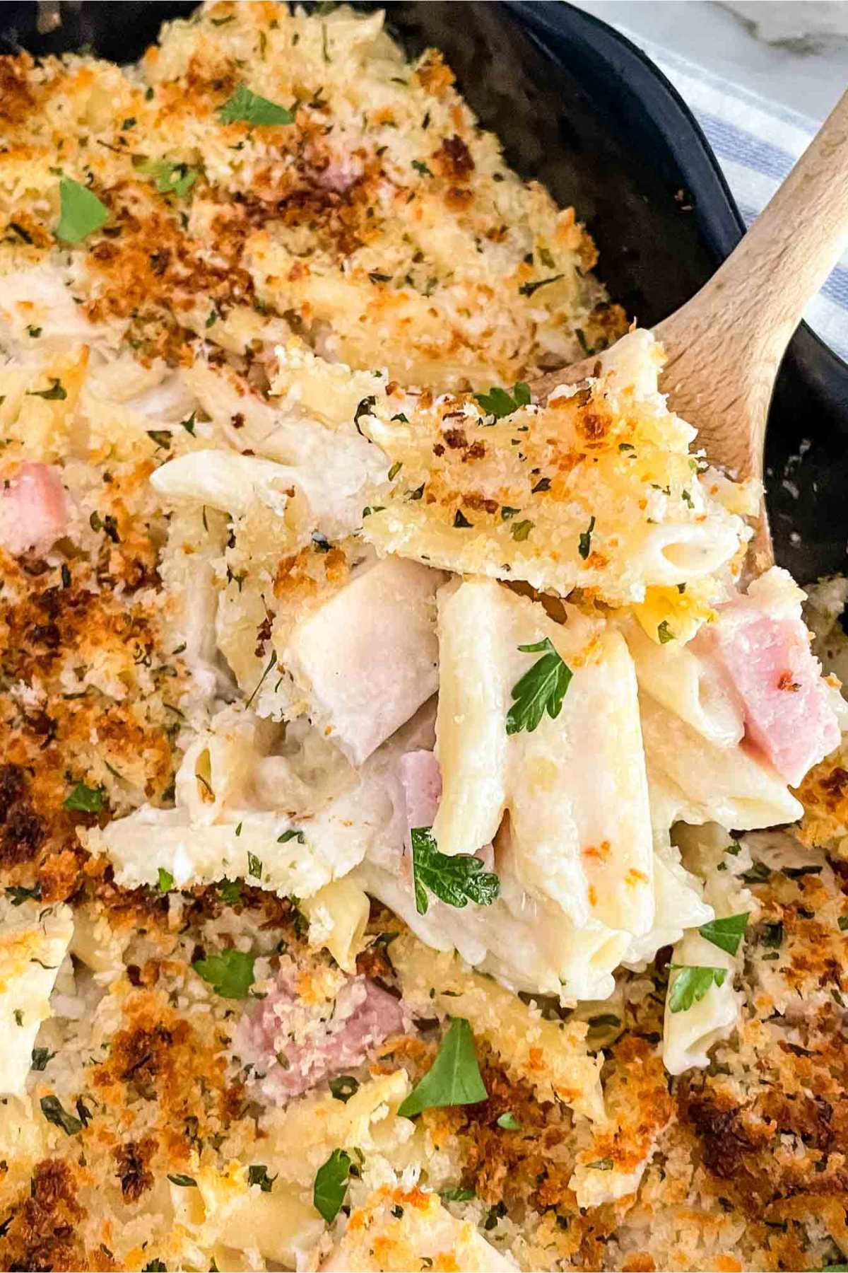 Chicken cordon bleu casserole pasta in a casserole dish with a wooden spoon scooping out a portion.