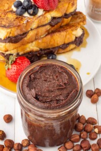 Jar of thick and creamy homemade hazelnut spread in front of a stack of french toast.