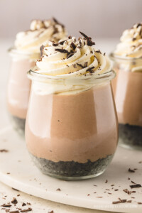 3 Curvy jars full of no bake nutella cheesecake topped with whipped cream and chocolate crumbles.